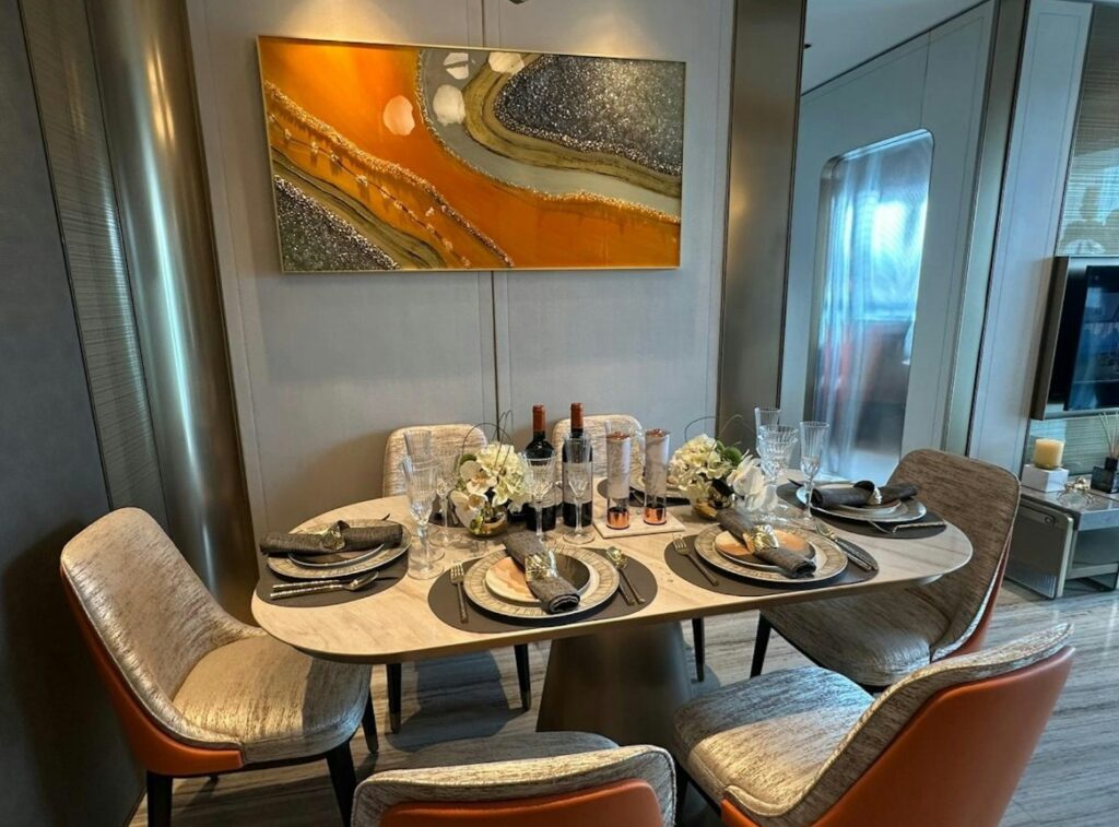維港‧灣畔第1B期 Victoria Voyage Phase 1B 現代餐廳設計，四人座圓形餐桌擺放高雅餐具與紅酒裝飾，牆上掛有橙色藝術畫作。